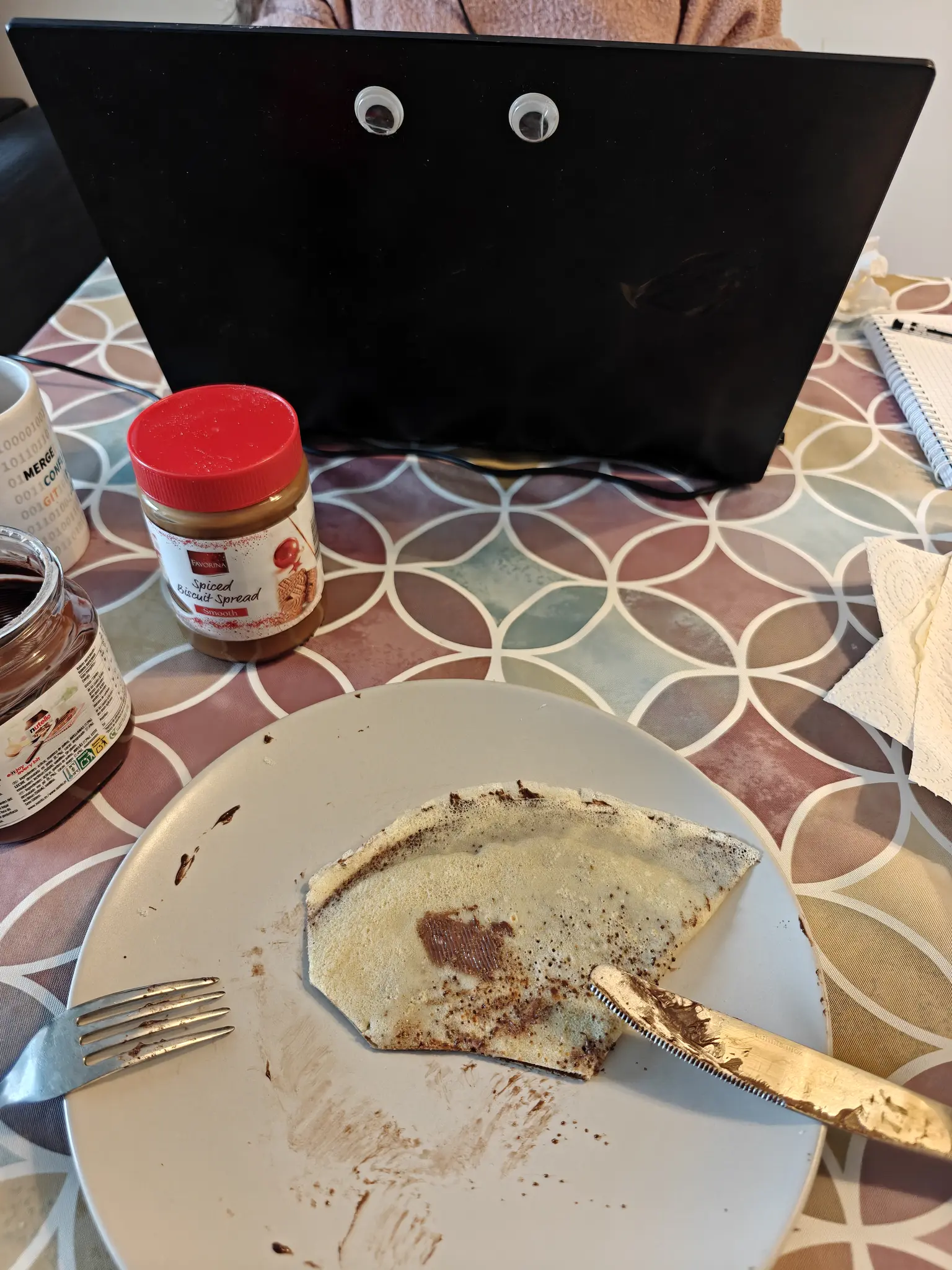 me eating some crepes in the table, with some fillings besides my plate, and Alba in front with a laptop that has googly eyes on the lid