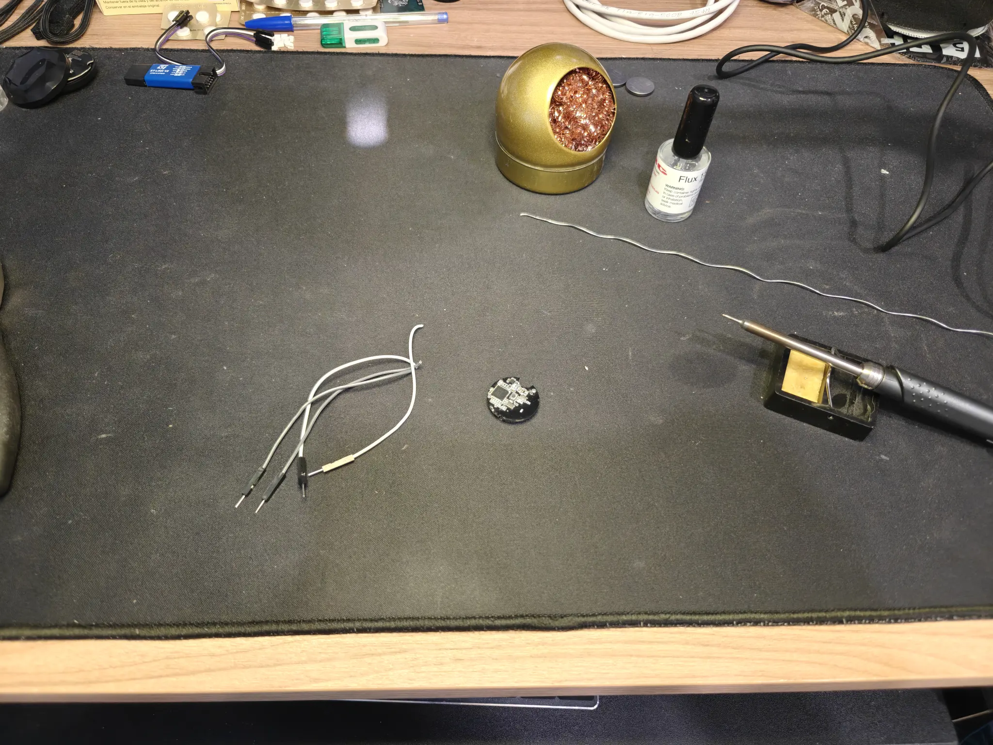 my desktop, with a black mat, and on top of it some soldering supply, a soldering iron, the Bluetooth tag, and some jumper cables cut in half