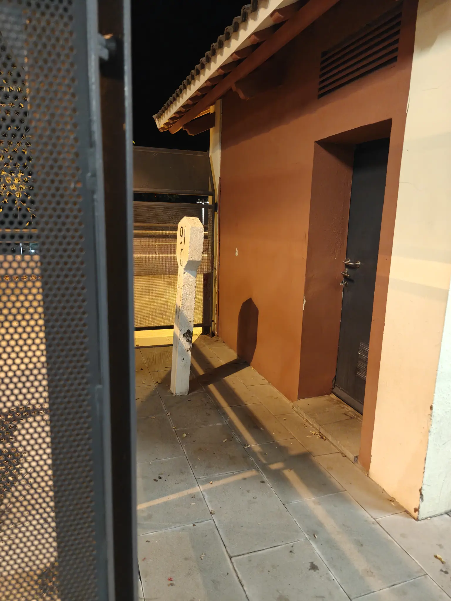 a milestone saying "91 0" in between a building and a fence