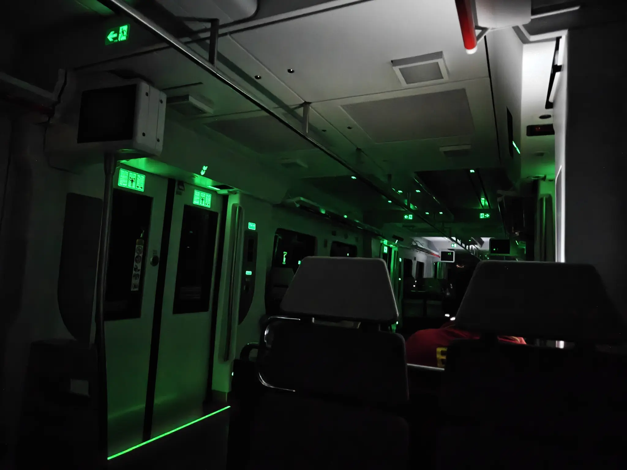 interior of Rodalies 447 with the lights completely off. only some emergency lights and UV-fluorescent stickers are visible