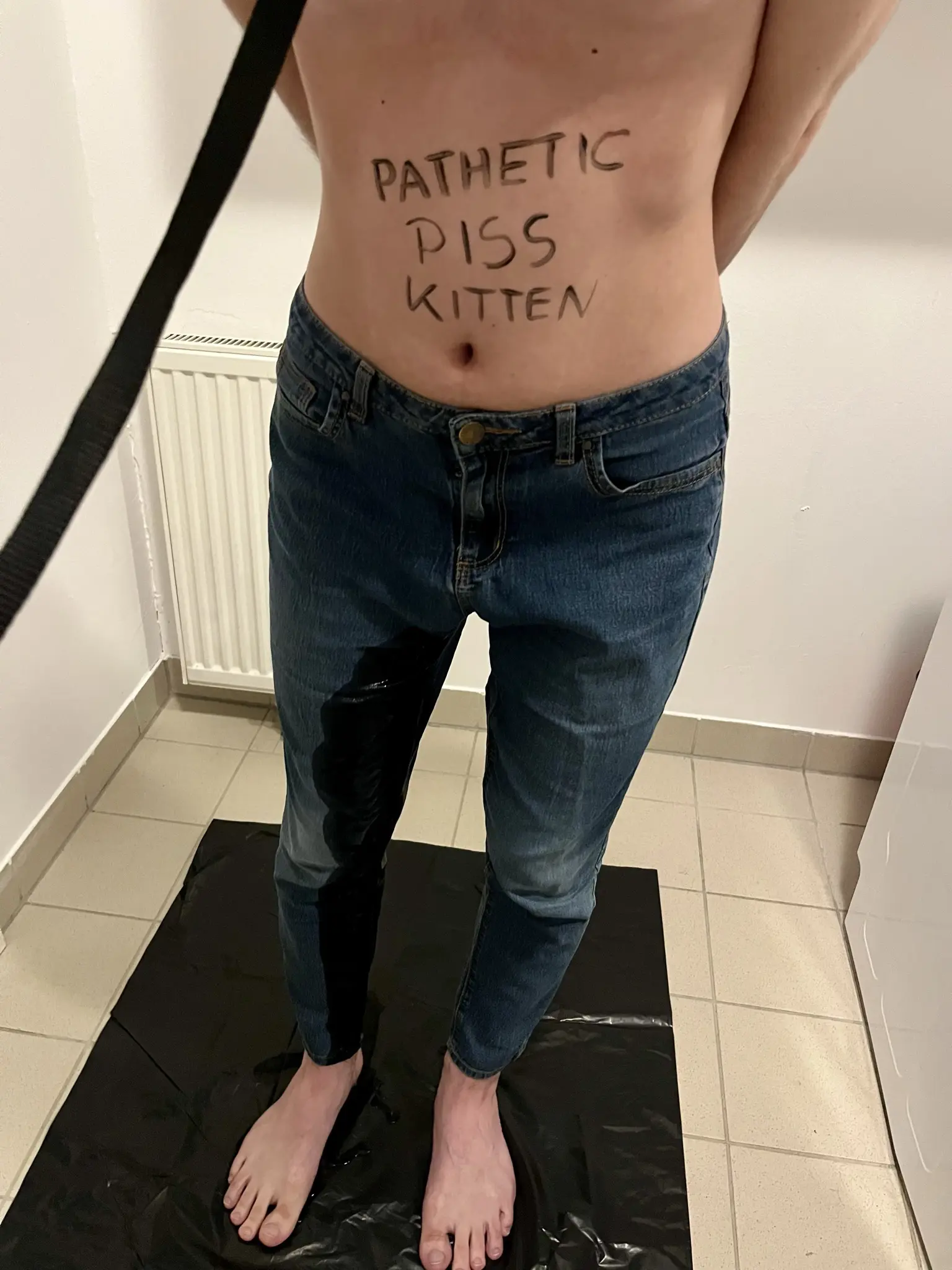 A close-up of the lower half of my body, from my tummy below. the writing in my stomach is visible on the top of the picture, and a big piss stain is visible in my right leg, going all the way from my crotch to the foot, with a puddle starting to form there