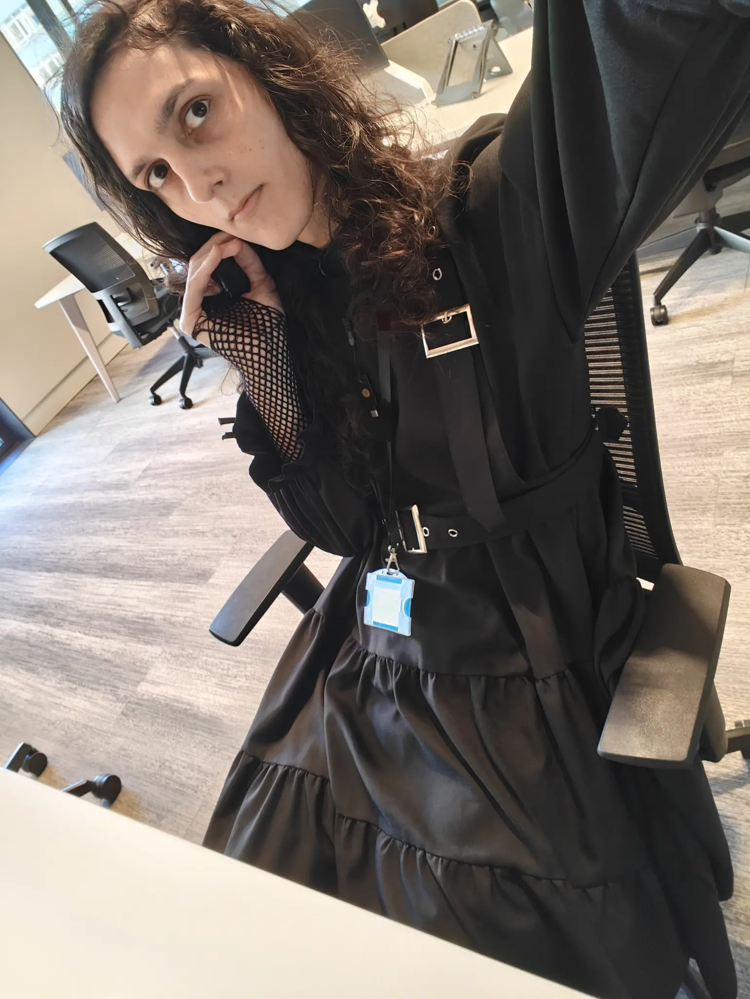 kitten in their office, sitting in front of a white desk, wearing a full black kinda goth looking dress, with an access card hanging from their neck